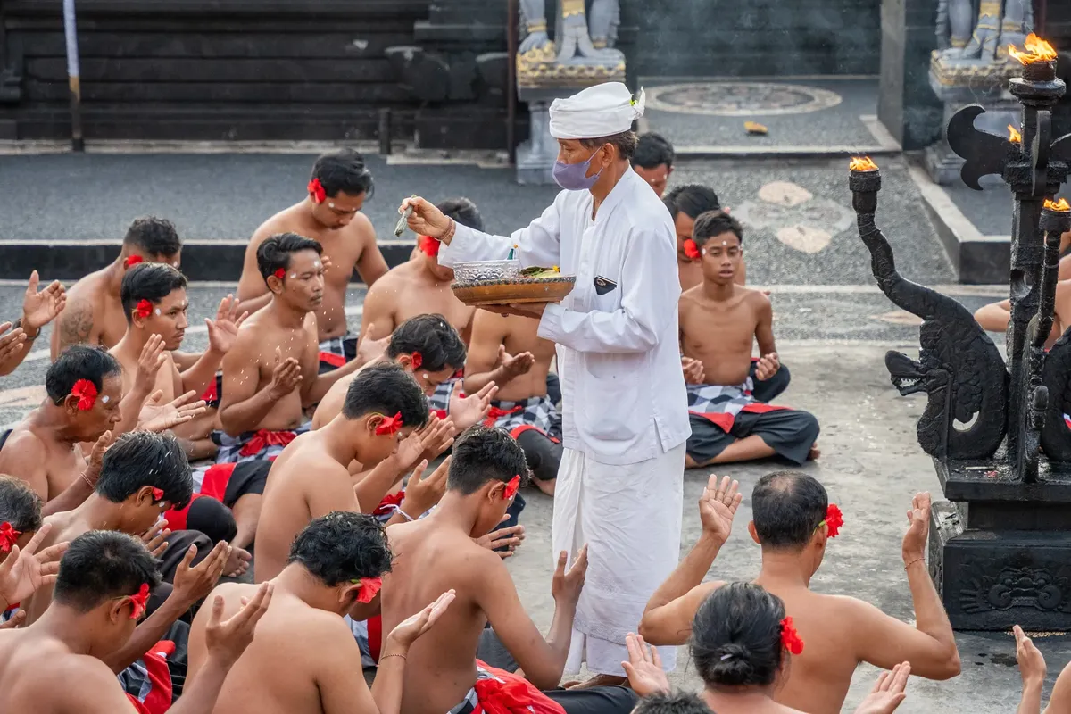 Group of men participate in a Bali temple ritual, led by a priest.