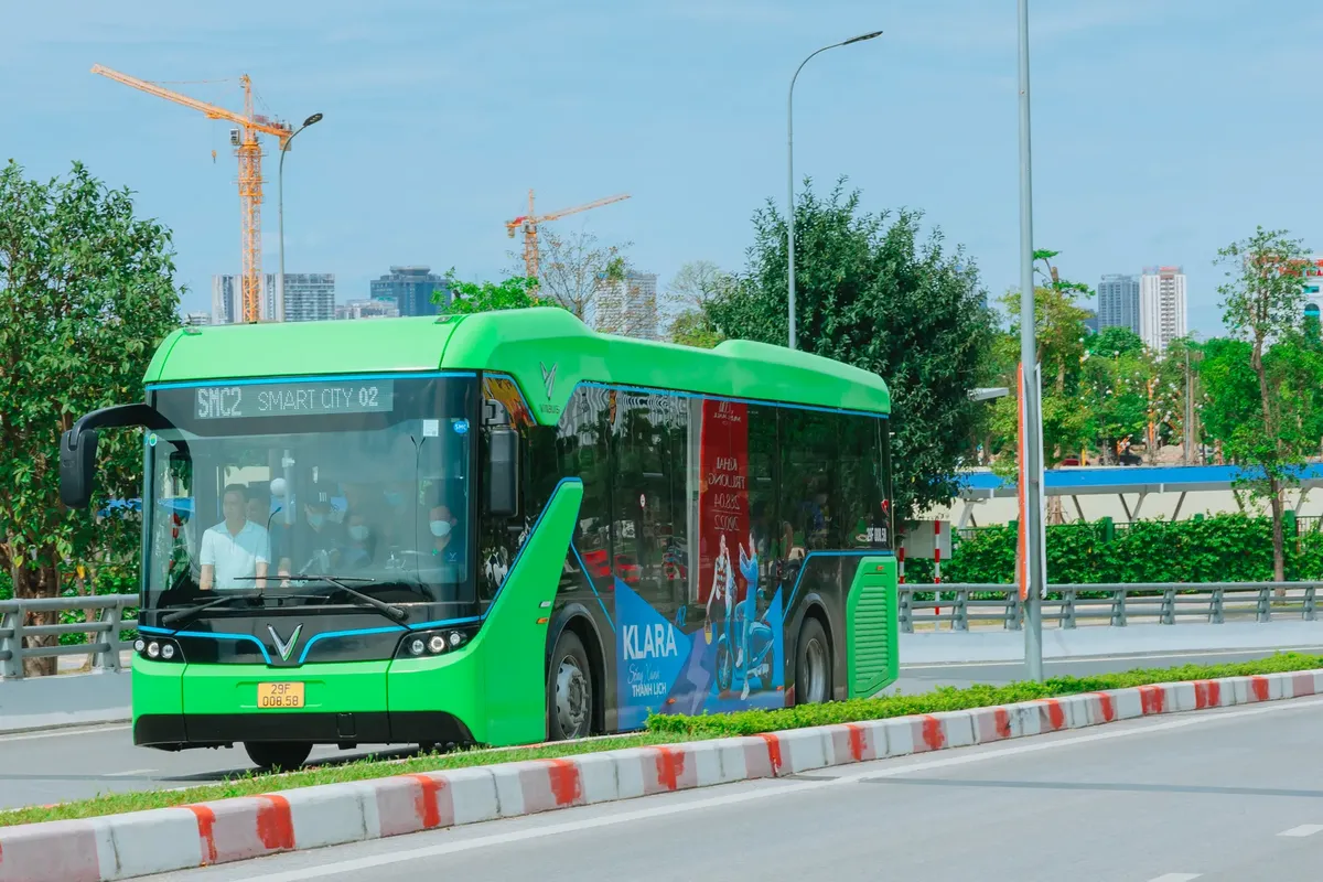 A modern green electric bus travels through Hanoi, showcasing urban transportation and city infrastructure.