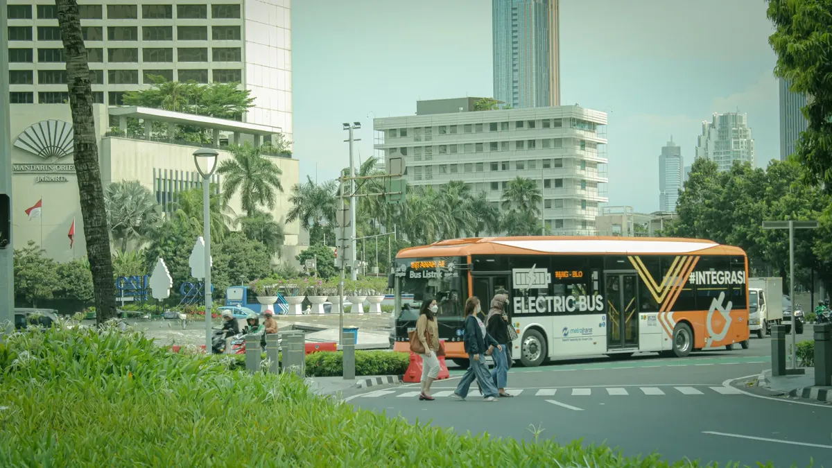 Electric bus on city street in Jakarta, Indonesia amidst urban traffic and pedestrians.